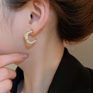 Detailed close-up of C-shaped gold hoop earrings with white pearls on female model