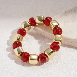 Detailed macro of a red glitter bead and gold metal cube bracelet on stone background