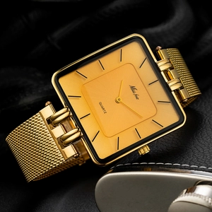 Detail of square gold watch with mesh strap placed next to a silver flask on leather