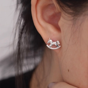 Close-up of a silver rocking horse stud earring with a textured finish on a model's ear