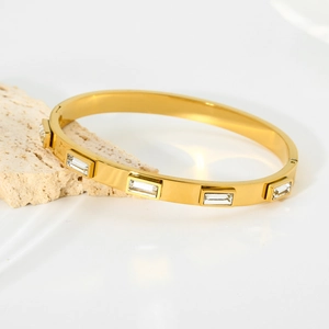 Gold-plated stainless steel oval bangle with five rectangular zirconia stones on white stone