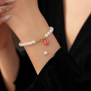Gold plated pearl bracelet with cute pink dragon fruit enamel charm on a model's wrist