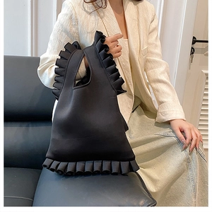 Detail of black ruffled handbag with pleated texture carried by a model in casual attire