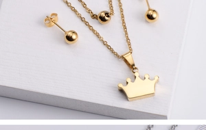 Detail showing a golden crown pendant necklace and bead earrings set on a stone base