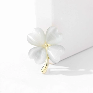 Elegante spilla a quadrifoglio dorata con petali di opale bianco su sfondo bianco neutro