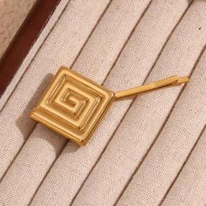 Détail macro d'une barrette dorée 18K avec motif géométrique de clé grecque
