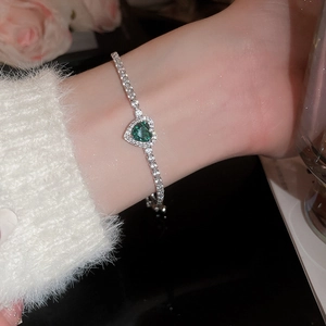 Detail of a silver tennis bracelet with a green heart crystal and pavé rhinestones