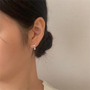 Close-up of silver bow earrings with teardrop zircon pendant worn by a model