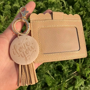 Close-up of beige leather card holder with tassel, gold keyring, and engraved charm