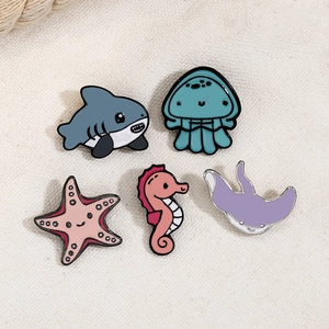 Detailed view of five ocean creature enamel pins on beige linen fabric background