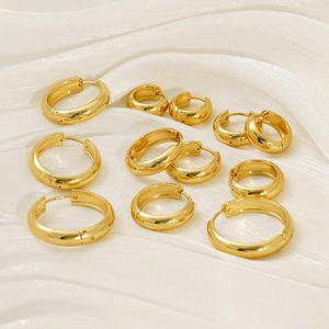 Macro shot of assorted sizes of polished golden hoop earrings on elegant white silk fabric