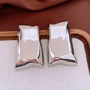 Detailed close-up of wavy liquid metal silver earrings on a wooden jewelry display