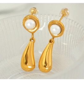 Detailed view of elegant gold water drop earrings with white pearls on a glass rim