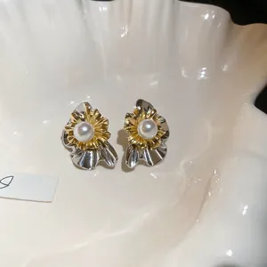 Close-up of pearl stud earring with golden flower petals on a white shell background