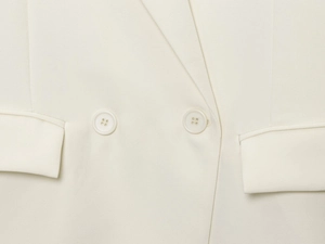 Détail du blazer blanc crème montrant les boutons à double boutonnage et la texture du tissu