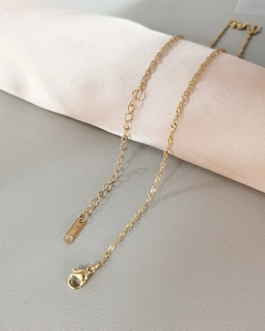 Macro detail of golden water wave chain with lobster clasp and S.STEEL stamp on silk