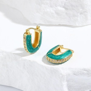 Macro detail of U-shaped gold earrings with green enamel and white zircon stones