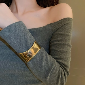 Close-up of a wide polished gold metal cuff bracelet styled over a grey knit sleeve