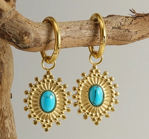 Détail de boucles d'oreilles tournesol en acier avec turquoise sur une branche en bois