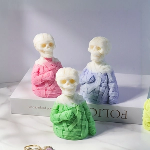 Three mummy skull candles in pink, green, and purple with bandage textures on a white book
