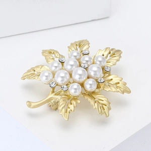 Golden leaf brooch with white pearls and small clear rhinestones on white background