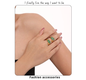 Détail d'une bague ouverte dorée ornée de zircons verts portée par un mannequin