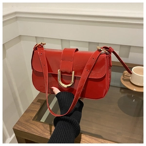Close-up of red patent leather shoulder bag with elegant golden U-shaped buckle detail
