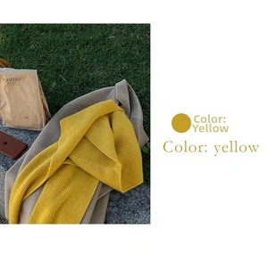 Detail of yellow ribbed knit hooded scarf paired with a camel coat in outdoor setting