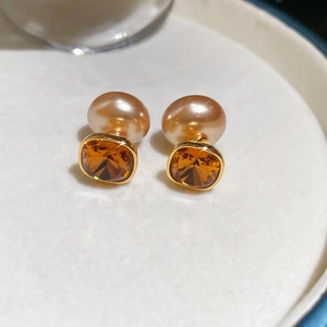 Macro shot of 18K gold-plated earrings with pearls and amber-colored square crystals