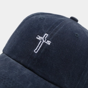 Detailed macro view of white cross embroidery on vintage washed blue cotton baseball cap