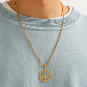 Close-up of a gold peace symbol pendant on a box chain worn over a blue sweatshirt