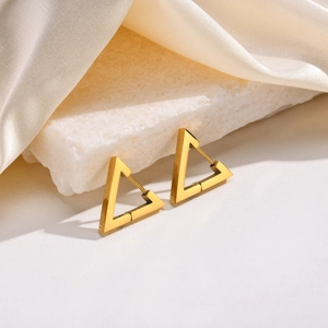 Macro detail of gold triangular hoop earrings on stone with white silk background
