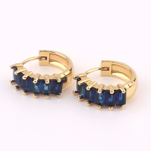 Close-up of golden hoop earrings featuring baguette-cut blue gemstones on pink background