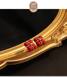 Macro view of vintage flower stud earrings with red beads and 18k gold plating on a mirror