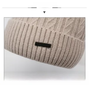 Detail view of the thick knit texture and metal logo plaque on a beige winter beanie hat