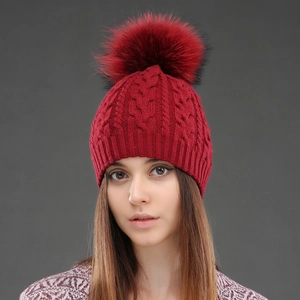 Close-up of deep red cable knit wool beanie featuring a real raccoon fur pom-pom