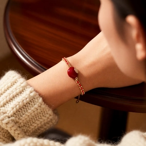 Nahaufnahme des 18k vergoldeten Armbands mit dunkelroten Perlen und Herzanhänger am Model
