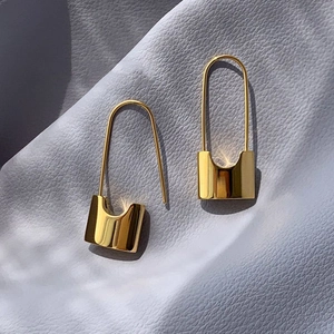 Detail showing golden lock-shaped earrings on a textured surface with natural sunlight