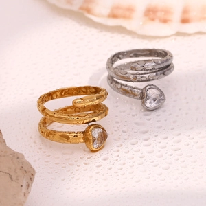 Detail of 18K gold and silver snake rings with heart zircon on watery stone background