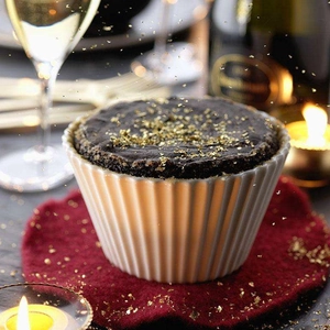 Edible gold foil flakes decorating a chocolate souffle cake in a white ceramic ramekin