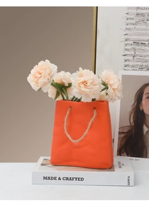 Close-up of orange ceramic shopping bag vase with jute rope handle and pink peony flowers
