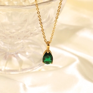 Macro shot of 18K gold plated necklace with green teardrop zircon pendant on white silk