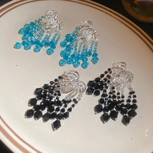 Detailed view of layered blue and black crystal beaded tassel earrings on a ceramic dish