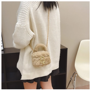 Detail of plush beige crossbody bag with gold rose pendant on white sweater