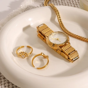 Set elegante con orologio in acciaio dorato, anelli e collana in un piatto di ceramica
