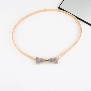 Detail of gold metal spring waist belt featuring a sparkling rhinestone bow buckle