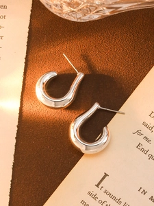 Close-up of silver C-shaped wavy irregular earrings on a vintage paper background