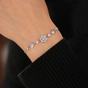 Detail of silver flower bracelet with sparkling zircons worn over a black knitted cuff