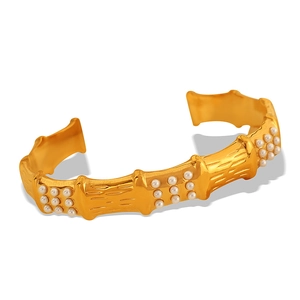 Golden bamboo-style cuff bracelet with small white pearls on a minimalist background