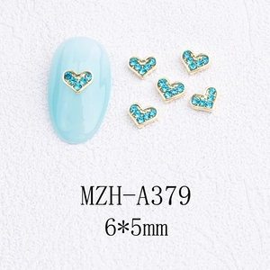 Détails macro de bijoux d'ongles cœur dorés avec strass bleus en taille 6x5mm
